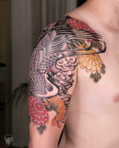 Japanese crane tattoo with red and yellow chrysanthemums on shoulder from Names Tattoo Studio in Lisbon