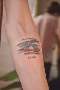 Micro-realism autumn maple leaf tattoo on the inner wrist, featuring a vibrant gradient of green, yellow, orange, and red with delicate stem detail