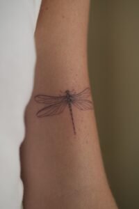 Micro-realism autumn maple leaf tattoo on the inner wrist, featuring a vibrant gradient of green, yellow, orange, and red with delicate stem detail