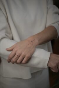 A fine-line Sanskrit script tattoo on the forearm featuring an Om symbol inside a sunburst, a blooming lotus flower, and delicate ornamental swirls, crafted at Names Tattoo Studio in Lisbon