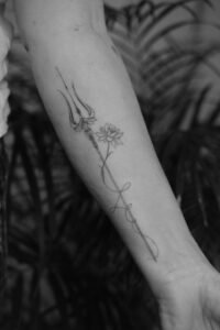 Fine line trident and lotus flower forearm tattoo with delicate script details