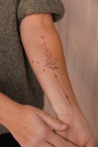 Fineline celestial forearm tattoo featuring planets, moon, and constellations