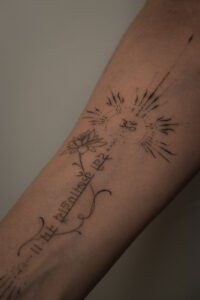 A surreal black and grey micro-realism tattoo on a leg featuring an Arowana fish spiraling around a vertical needle, complemented by abstract geometric shards at the top