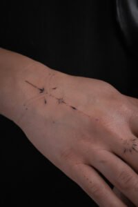 Fine line celestial hand tattoo featuring stars, crescent moon, and dainty dots