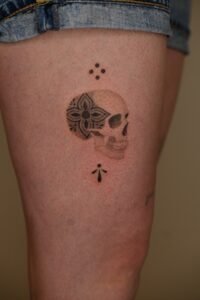 Small fineline skull tattoo with floral mandala detail on thigh