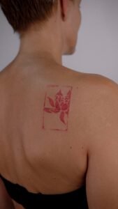 A surreal black and grey micro-realism tattoo on a leg featuring an Arowana fish spiraling around a vertical needle, complemented by abstract geometric shards at the top