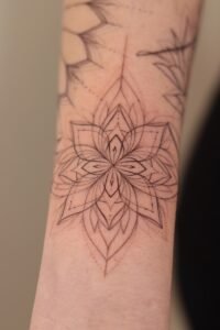 Fine line mandala tattoo on the inner forearm featuring symmetrical lotus-inspired geometric patterns and delicate dotwork details