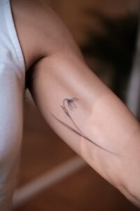 Minimalist fine line snowdrop flower tattoo with delicate shading on the inner bicep