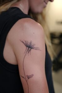 A surreal black and grey micro-realism tattoo on a leg featuring an Arowana fish spiraling around a vertical needle, complemented by abstract geometric shards at the top