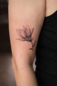 Micro-realism autumn maple leaf tattoo on the inner wrist, featuring a vibrant gradient of green, yellow, orange, and red with delicate stem detail