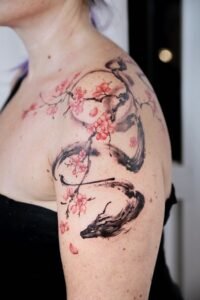 Sumi-e style dragon and cherry blossom tattoo on the shoulder and upper arm, featuring a black ink brushstroke dragon entwined with delicate pink sakura flowers