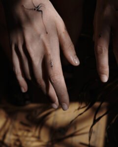 Micro-realism autumn maple leaf tattoo on the inner wrist, featuring a vibrant gradient of green, yellow, orange, and red with delicate stem detail