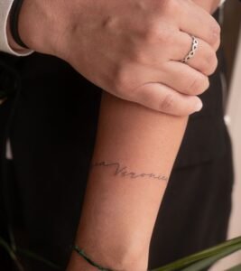 Minimalist cursive name tattoo featuring the name Veronica in an elegant fine line script wrapping around the forearm