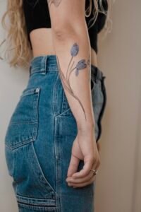 Elegant blue tulip forearm tattoo in fine line style from Names Tattoo Studio in Lisbon