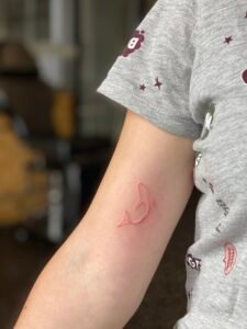 Blue ink ornamental tattoo inspired by azulejo Portuguese tile patterns, featuring a symmetrical diamond-shaped design with intricate fine-line scrolls and floral motifs on the skin