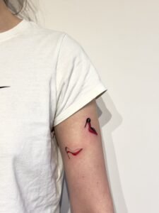 A surreal black and grey micro-realism tattoo on a leg featuring an Arowana fish spiraling around a vertical needle, complemented by abstract geometric shards at the top